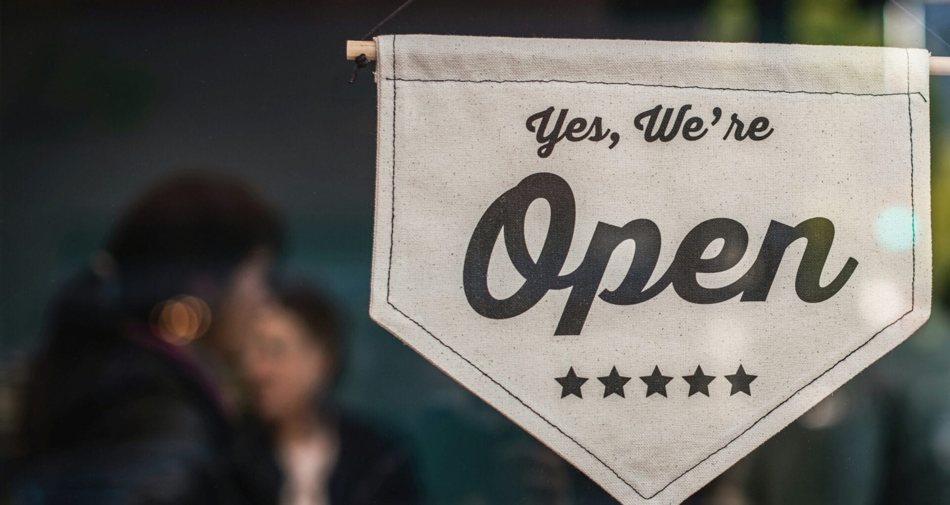 "Yes, we're open" fabric pennant sign hanging in a storefront window