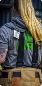 Rear view of a firefighter at a fire scene wearing a protective hood and turnout pants with SCBA straps visible