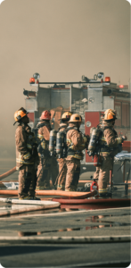 Group of four firefighters in full gear gathered near a fire engine in hazy conditions