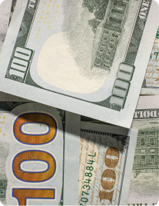 Close-up of overlapping U.S. $100 bills, showing detailed security features and printed numerals.
