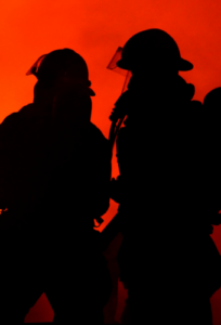 Fire trucks lined up on a street at night with flashing red lights, firefighters and equipment visible between them.