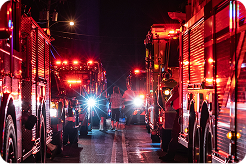 Fire engines at night illuminated by their headlights and emergency lights, with wet pavement reflecting