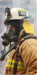 Firefighter in full turnout gear and oxygen mask, with heavy smoke behind him