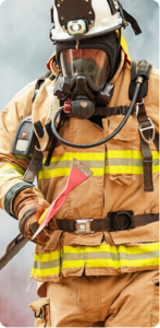 Fireman in turnout gear and oxygen mask walking towards the camera, holding a fire axe