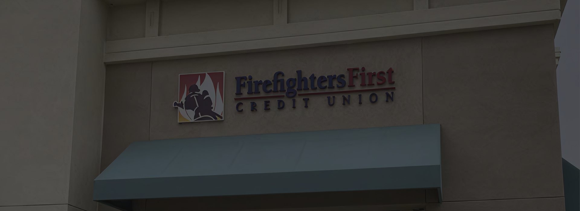 Exterior of the Firefighters First Credit Union Loma Linda branch, featuring a tan stucco building with the FFCU logo and wordmark mounted above a blue awning over the entrance.