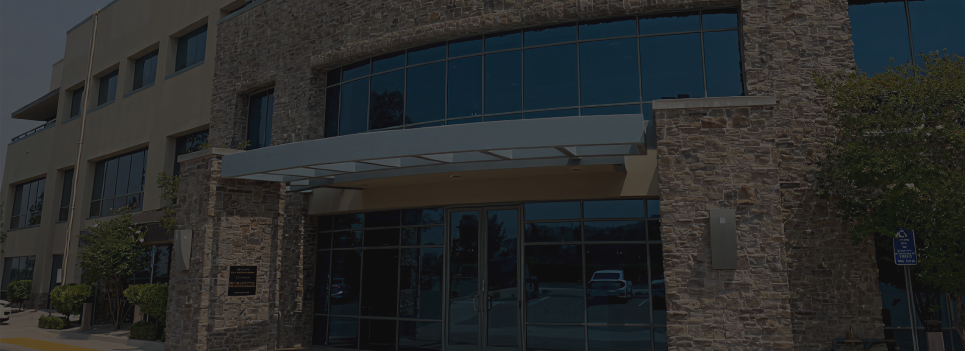 Exterior of the Firefighters First Credit Union Santa Clarita branch, a multi-story building with a stone facade, curved glass curtain wall and a covered entrance canopy.