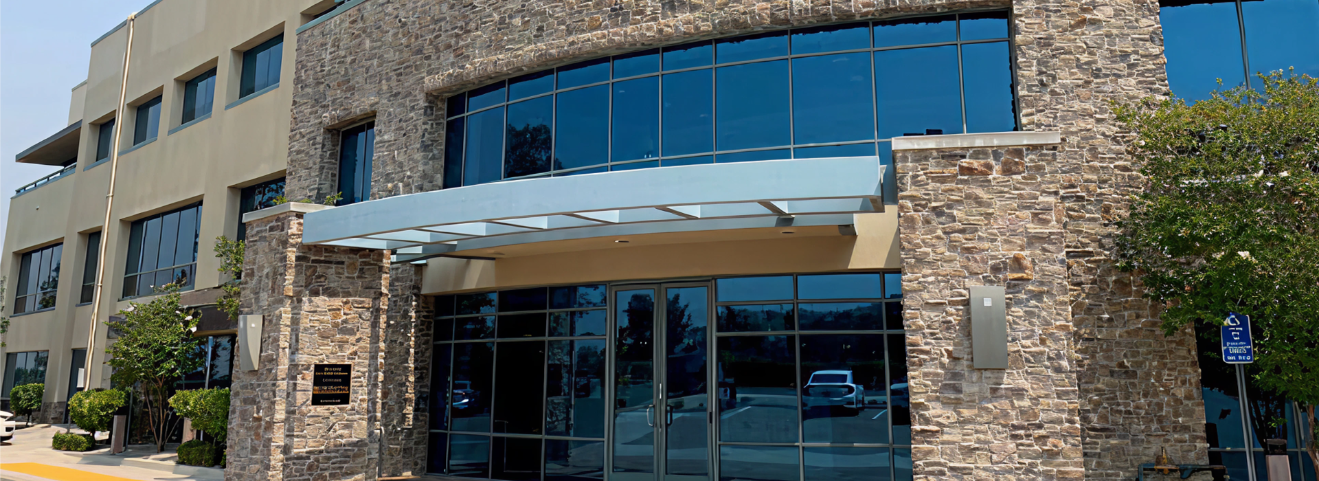 Exterior of the Firefighters First Credit Union Santa Clarita branch, a multi-story building with a stone facade, curved glass curtain wall and a covered entrance canopy.