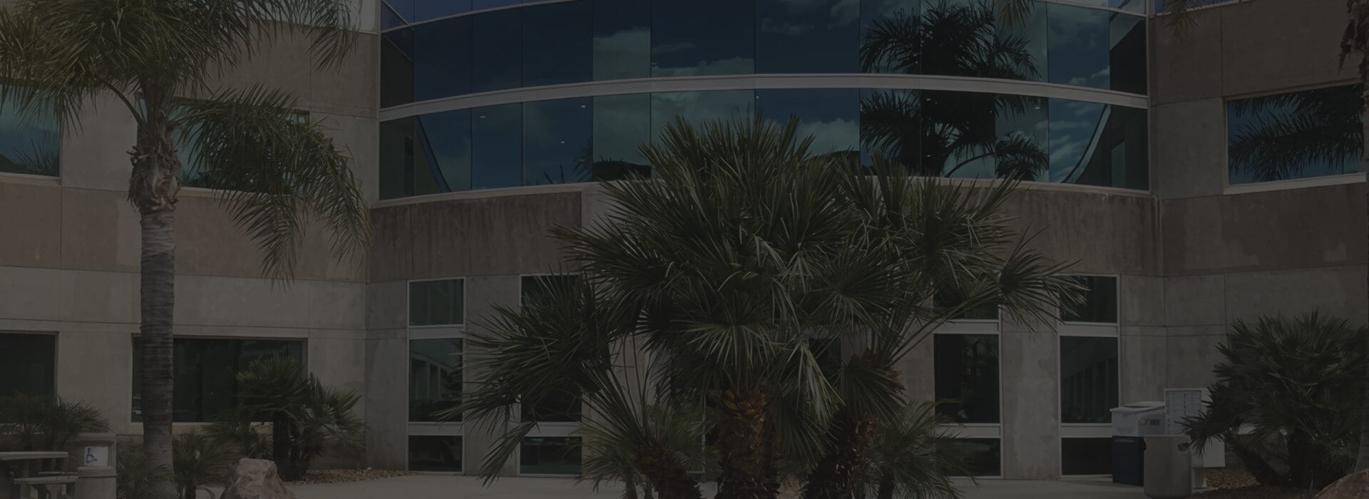 Exterior of the Firefighters First Credit Union Temecula branch, a curved multi-story office building with reflective blue glass windows and palm trees in the foreground.