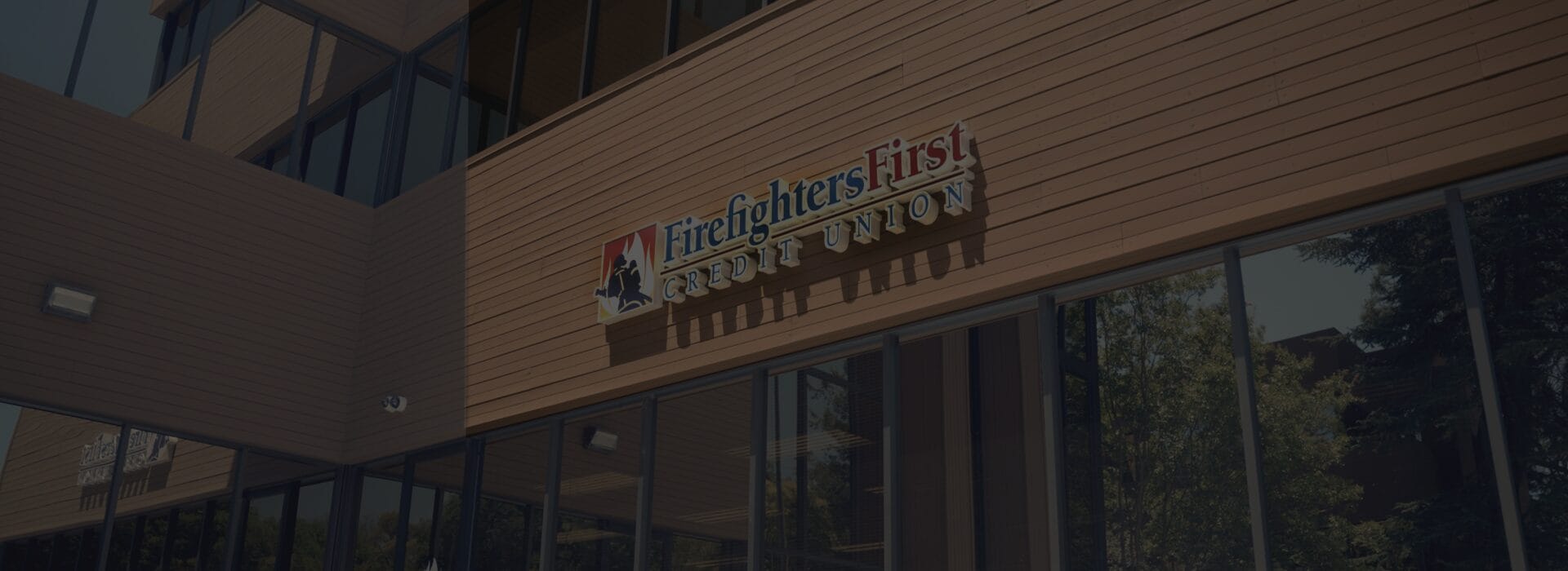 Exterior of the Firefighters First Credit Union Walnut Creek branch, featuring a modern building with warm wood siding and the FFCU logo and wordmark mounted above large glass windows.