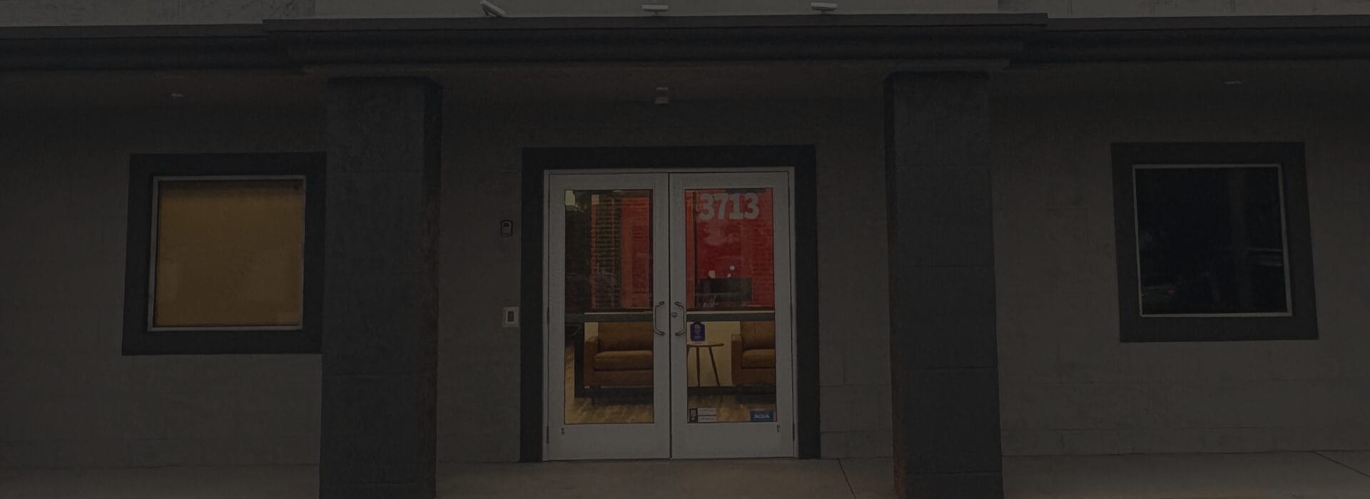 Exterior entrance of the Firefighters First Credit Union West Palm Beach branch, featuring glass double doors with the number 3713 and interior seating visible through the windows.